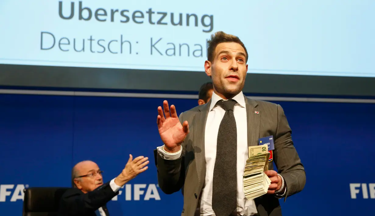Komedian asal Inggris, Lee Nelson memegang uang kertas di depan Presiden FIFA Sepp Blatter (kiri) saat konferensi pers di markas FIFA di Zurich, Swiss (20/7/2015). Kedatangan Nelson membuat jumpa pers tertunda beberapa saat. (REUTERS/Arnd Wiegmann)
