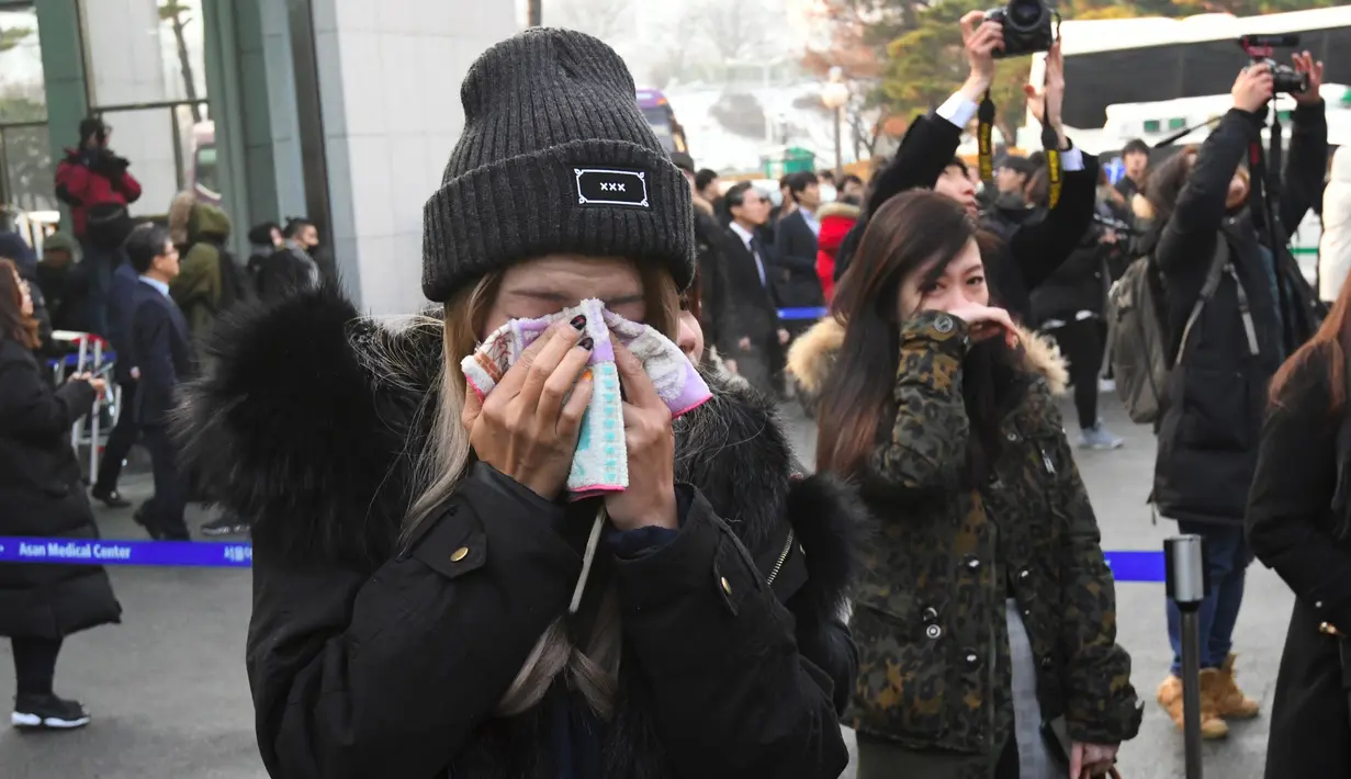 Seorang fans menangis saat mobil yang membawa jenazah Jonghyun SHINee keluar dari rumah persemayaman di Asan Hospital, Seoul menuju tempat pemakaman, Kamis (21/12). Pihak keluarga tidak mempublikasikan lokasi pemakaman Jonghyun SHINee. (JUNG Yeon-Je/AFP)