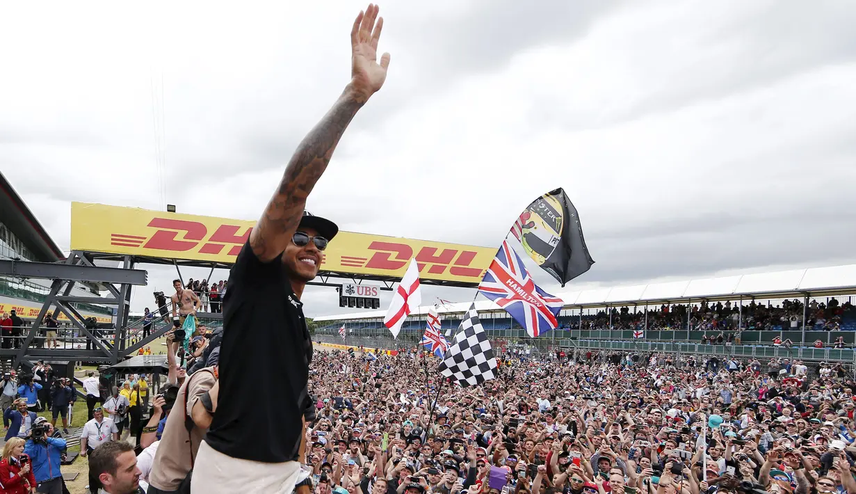 Pembalap Formula 1, Lewis Hamilton merayakan kemenangan bersama pengemarnya usai berlaga di Grand Prix Formula 1 Silverstone di Inggris, (5/7/2015). Hamilton berhasil finish di urutan pertama dengan waktu 1 jam 31 menit 27,729 detik. (Reuters/Hoch Zwei)