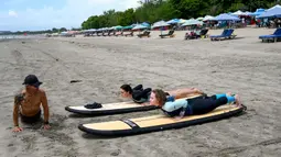 Seorang instruktur memberi contoh teknik berselancar di pantai Kuta, Bali, pada 8 Desember 2023. (SONNY TUMBELAKA/AFP)