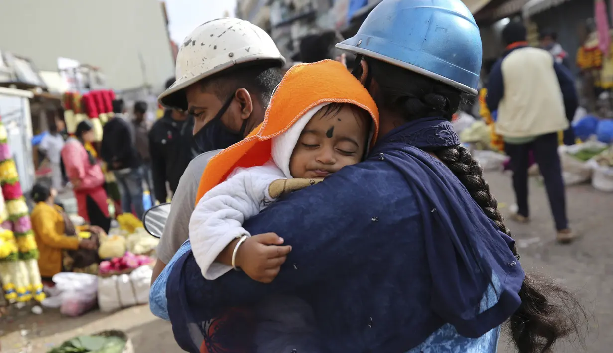 Seorang anak tertidur di pangkuan ibunya saat bepergian dengan skuter untuk berbelanja di pasar grosir bunga di Bengaluru, India, Kamis (24/9/2020). Negara berpenduduk 1,3 miliar itu diperkirakan akan menjadi negara terparah pandemi COVID-19 dalam beberapa minggu, melampaui AS. (AP Photo/Aijaz Rahi)
