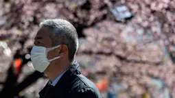 Seorang pria mengenakan masker melewati pohon sakura di taman Ueno, Tokyo (12/3/2020). Hingga Rabu (11/3), Otoritas Tokyo melaporkan 581 kasus, dengan 12 orang meninggal dan 101 sembuh. (AFP/Philip Fong)