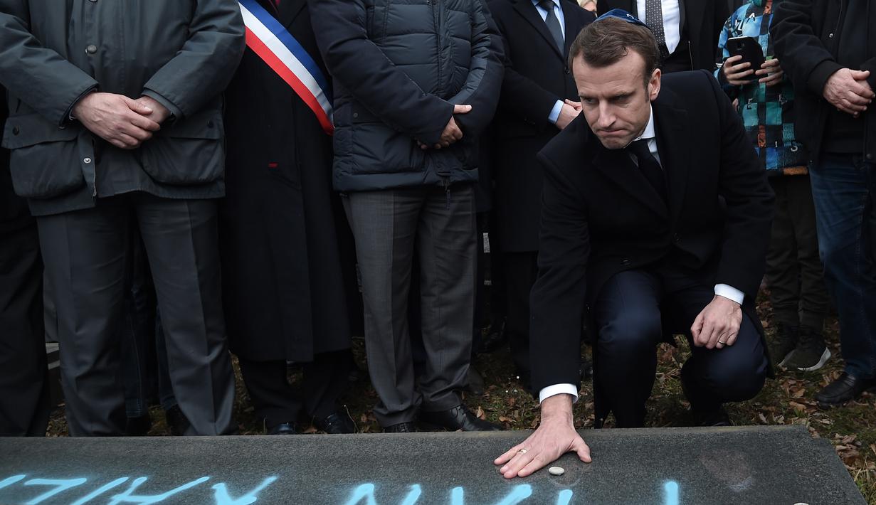 Presiden Prancis Emmanuel Macron meletakkan batu di atas makam Yahudi yang dicoret simbol Nazi di pemakaman Yahudi, Quatzenheim, Prancis, Selasa (19/2). Macron juga juga menyatakan akan menghukum para pelaku vandalisme. (Frederick FLORIN/AFP)