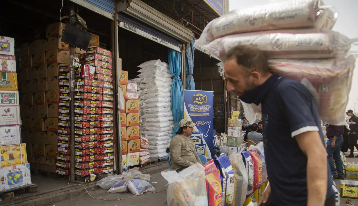 Pekerja memanggul bahan makanan di pasar Jamila Baghdad, Irak, Rabu, 9 Maret 2022. Harga makanan, bahan bakar, dan bahan konstruksi naik 20 hingga 50 persen di Irak, karena situasi perang saat ini di Ukraina. (AP Photo/Hadi Mizban)