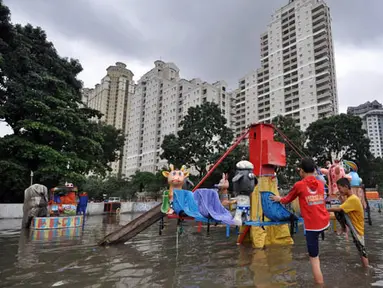 Sejumlah anak bermain di lahan bermain Kemayoran yang terendam banjir, Jakarta, Selasa (10/2). Tingginya curah hujan di wilayah Jakarta mengakibatkan sejumlah daerah masih terendam banjir. (Liputan6.com/Faizal Fanani)