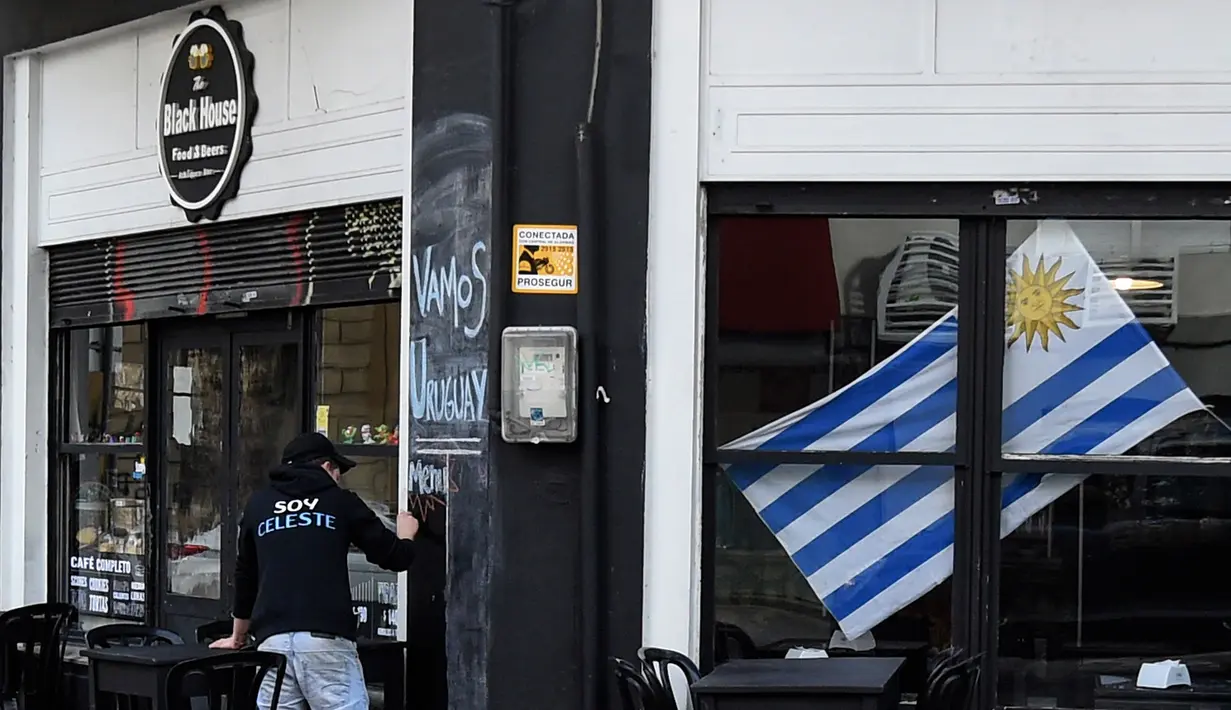 Bendera Uruguay dipajang dikaca di sebuah cafe Montevideo (4/7). Warga Uruguay antusias mempersiapkan untuk mendukung negaranya bertanding melawan Prancis pada babak 8 besar Piala Dunia 2018 di Rusia. (AFP Photo/Miguel Rojo)
