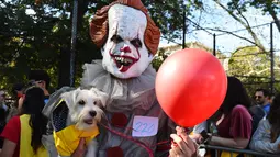 Seorang pria mengenakan kostum badut berpose dengan anjingnya saat Parade Halloween Anjing Tahunan di Tompkins, New York (21/10). Pemilik anjing juga ikut memakai kostum aneh untuk mengikuti parade ini. (AFP Photo/Timothy A. Clary)