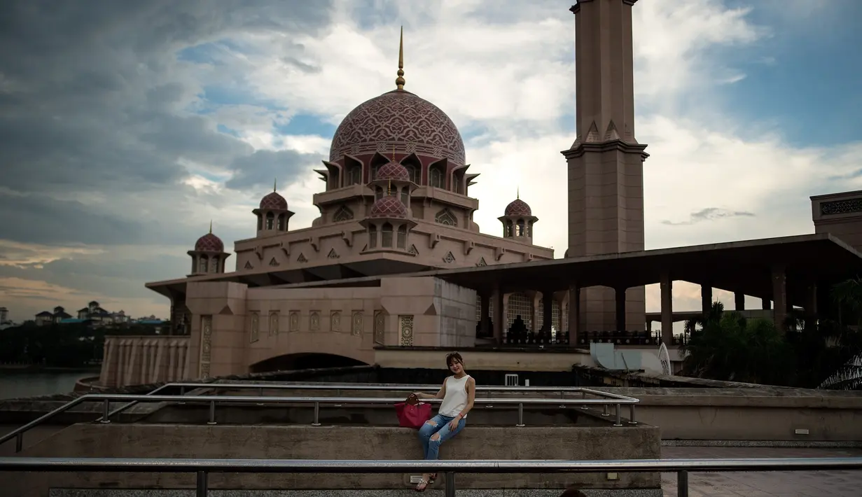 Gambar yang diambil pada 22 November 2017, memperlihatkan seorang turis berpose di depan masjid berwarna pink di kawasan Putrajaya, Malaysia. Masjid Putra ini terdiri dari 4 lantai yang dilengkapi dengan lift. (MANAN VATSYAYANA/AFP)