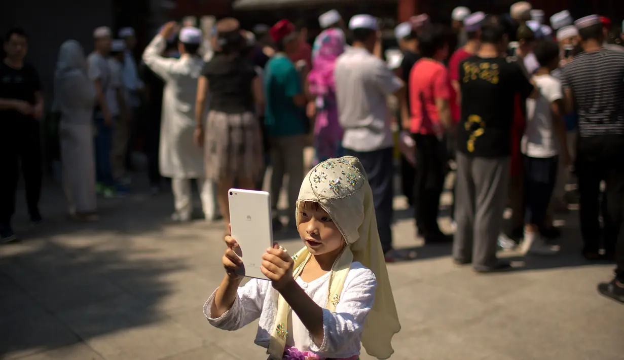 Seorang anak perempuan mengambil gambar seusai pelaksanaan salat Idul Fitri di masjid Niujie, Beijing, 26 Juni 2017. Umat muslim di berbagai penjuru dunia merayakan Idul Fitri, yang menandai berakhirnya bulan suci Ramadan. (AP Photo/Mark Schiefelbein)