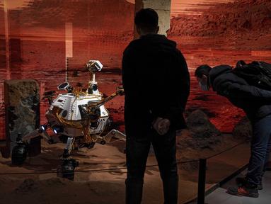 Pengunjung mengenakan masker untuk mencengah penyebaran Covid-19 melihat model yang menggambarkan penjelajah di Mars selama pameran di sebuah pusat perbelanjaan di Beijing, Rabu, (24/2/2021).  China mengatakan pesawat ruang angkasa Tianwen-1 telah memasuki masa temporer. (AP Photo/Andy Wong)