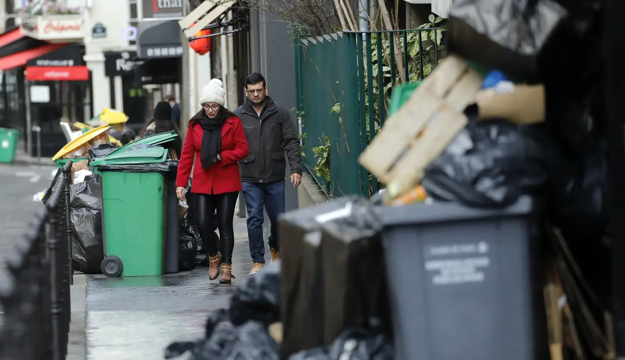 Orang-orang berjalan melewati tong sampah dan tumpukan kantong sampah yang menumpuk di Paris (4/2/2020). Serikat pekerja memutuskan kegiatan di pabrik pembakaran kunci untuk memprotes reformasi yang mereka katakan tidak adil. (AP Photo/Christophe Ena)