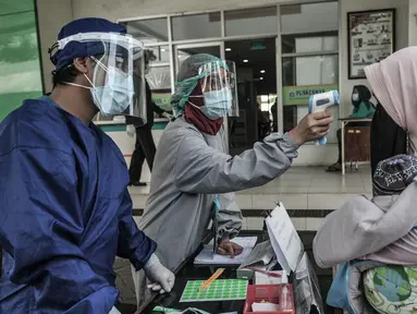 Petugas paramedis memeriksa suhu tubuh seorang ibu sebelum mengantarkan anaknya mengikuti imunisasi di Puskesmas Kecamatan Jatinegara, Jakarta, Kamis (26/11/2020). (merdeka.com/Iqbal S. Nugroho)