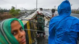 Penduduk desa mencoba untuk menyeberangi kabel listrik yang jatuh di jembatan dekat Diu setelah siklon Tauktae menghantam pantai barat India pada Selasa (18/5/2021). Topan Tauktae disebut yang terbesar melanda wilayah itu dalam beberapa dekade terakhir. (Punit PARANJPE / AFP)