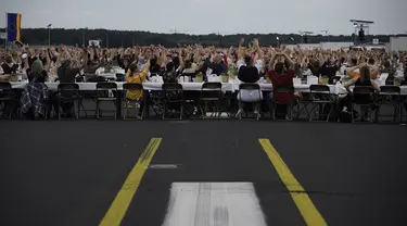 Para tamu melambai ke arah helikopter yang terbang di atas meja mereka saat acara “Berlin Freedom Dinner” di landasan pacu bekas bandara Tegel, Berlin pada 7 Agustus 2021. Acara itu untuk mengirim sinyal 'Berlin kembali!' setelah berbulan-bulan menghadapi pandemi COVID-19. (Tobias SCHWARZ/AFP)