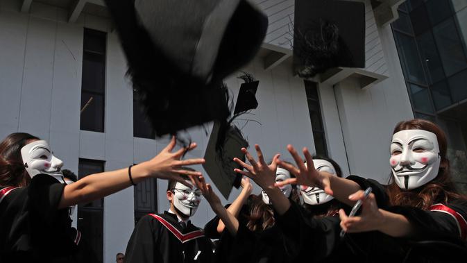 Wisudawan bertopeng Guy Fawkes melemparkan topi wisuda setelah upacara kelulusan mereka di Chinese University of Hong Kong, Hong Kong, Kamis (7/11/2019). Sekitar seribu mahasiswa mengabaikan larangan mengenakan topeng yang dikeluarkan pemerintah pada Oktober 2019. (AP/Kin Cheung)
