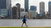 Seorang pria yang mengenakan masker berjalan di sepanjang tepi pantai di Perth (29/6/2021). Warga di Kota Perth, ibu kota Australia Barat, dan wilayah tetangga Peel harus tinggal di rumah kecuali untuk alasan mendesak. (AFP/Trevor Collens)