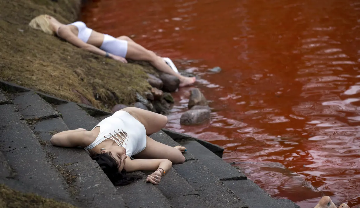 Orang-orang berbaring di tanah untuk melambangkan mereka yang tewas dalam perang di Ukraina selama protes terhadap invasi Rusia, di dekat kolam berwarna merah untuk menandakan darah di depan kedutaan besar Rusia di Vilnius, Lithuania, Kamis (7/4/2022). (AP Photo/Mindaugas Kulbis)