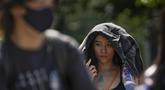 Seorang wanita menggunakan jaketnya untuk melindungi dari sinar matahari berjalan di sepanjang jalan saat ibu kota dilanda gelombang panas di Beijing, Senin, 5 Juni 2023. (AP Photo/Andy Wong)
