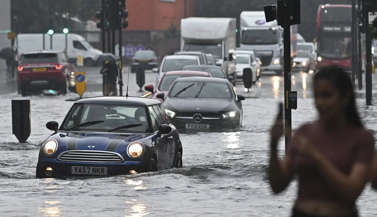 Mobil melintasi jalan yang banjir saat hujan lebat di distrik The Nine Elms London (25/7/2021). Banjir parah terjadi di Ibu Kota Inggris London yang menyebabkan lumpuhnya sejumlah area di kota tersebut. (AFP/Justin Tallis)