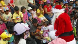 Seorang petugas polisi berpakaian seperti Santa Claus memberikan hadiah kepada anak-anak selama perayaan Natal di Huaycan, Lima, Peru (15/12/2015). (REUTERS/Janine Costa)
