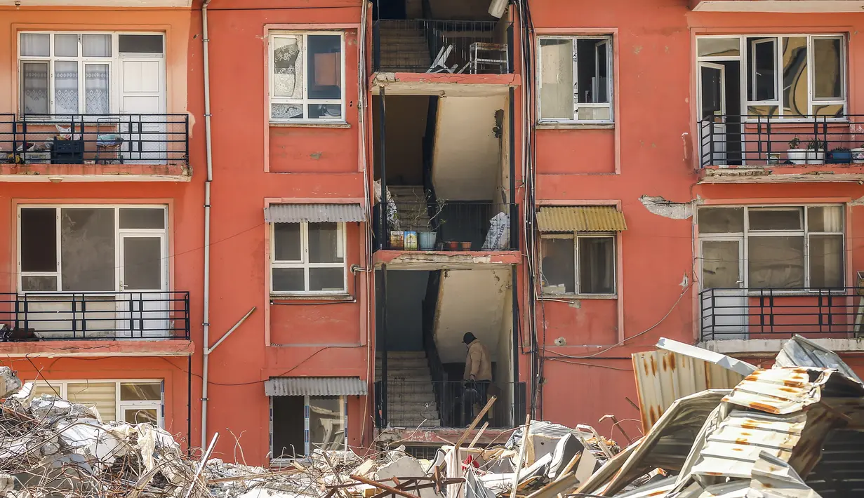 Seorang pria menaiki tangga blok apartemen yang rusak sebagian di samping bangunan yang hancur pascagempa di Samandag, Turki selatan, Rabu, 22 Februari 2023. Korban selamat dari gempa yang mengguncang Turki dan Suriah 15 hari lalu, menewaskan puluhan ribu orang dan menyebabkan ratusan ribu lainnya kehilangan tempat tinggal , menghadapi lebih banyak trauma dan kehilangan setelah gempa mematikan dan gempa susulan mengguncang wilayah tersebut. (AP Photo/Emrah Gurel)
