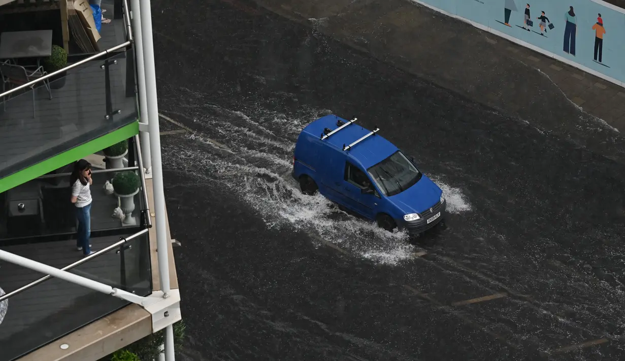 Seorang wanita melihat van melintasi banjir saat hujan lebat di distrik The Nine Elms London (25/7/2021). Bus dan mobil terjebak banjir ketika jalan-jalan di London banjir pada hari Minggu, ketika badai petir berulang kali melanda ibu kota Inggris. (AFP/Justin Tallis)