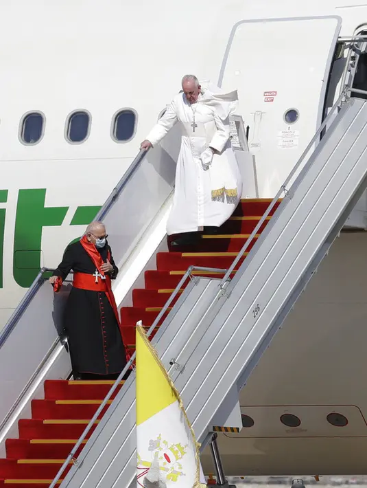 Paus Fransiskus berjalan menuruni tangga pesawat saat tiba di Bandara Internasional Baghdad, Irak, Jumat (5/3/2021). Paus Fransiskus datang ke Irak untuk mendesak umat Kristen tetap tinggal dan membantu membangun kembali Irak setelah bertahun-tahun perang. (AP Photo/Andrew Medichini)