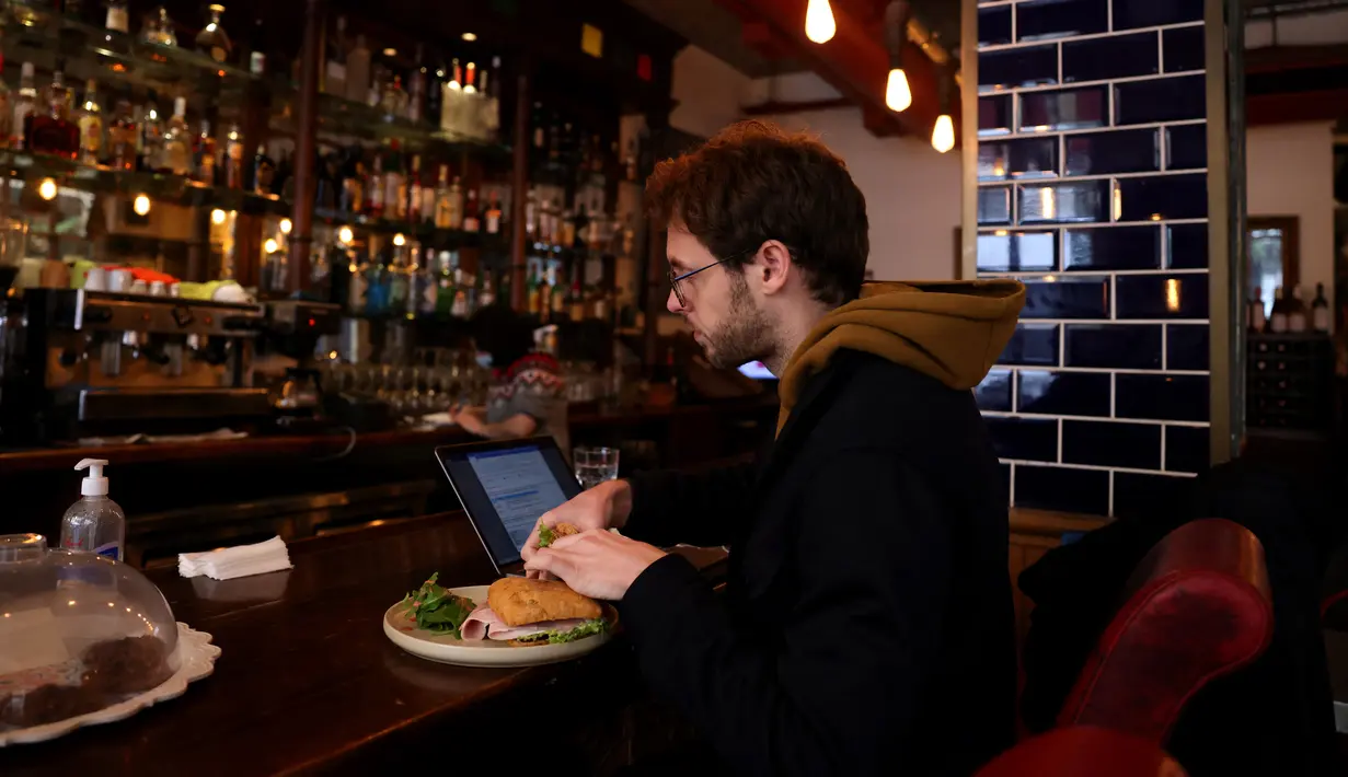 Seorang pria makan di samping laptopnya di sebuah kafe di Beirut pada 14 Januari 2022. Kafe-kafe Beirut sekarang berfungsi sebagai tempat kerja pengganti bagi orang-orang yang bergulat dengan kekurangan listrik dan pemutusan internet yang berasal dari krisis ekonomi. (JOSEPH EID / AFP)