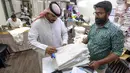 Seorang penjahit menyerahkan pesanan "dishdashas" kepada pelanggan, pakaian tradisional Kuwait, setelah menunggu selama satu setengah bulan di tengah tingginya permintaan saat pertemuan sosial dilanjutkan di bulan suci Ramadhan, di sebuah toko di Kota Kuwait, Minggu (2/4/2023). (YASSER AL-ZAYYAT/AFP)