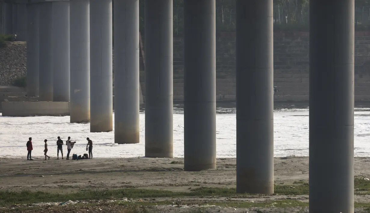 Para pemuda membuka pakaiannya sebelum berendam di sungai Yamuna yang tercemar di bawah jembatan di pinggiran New Delhi (23/7/2020). Sungai ini menyandang gelar sebagai sungai paling tercemar di dunia. (AFP Photo/Xavier Galiana)