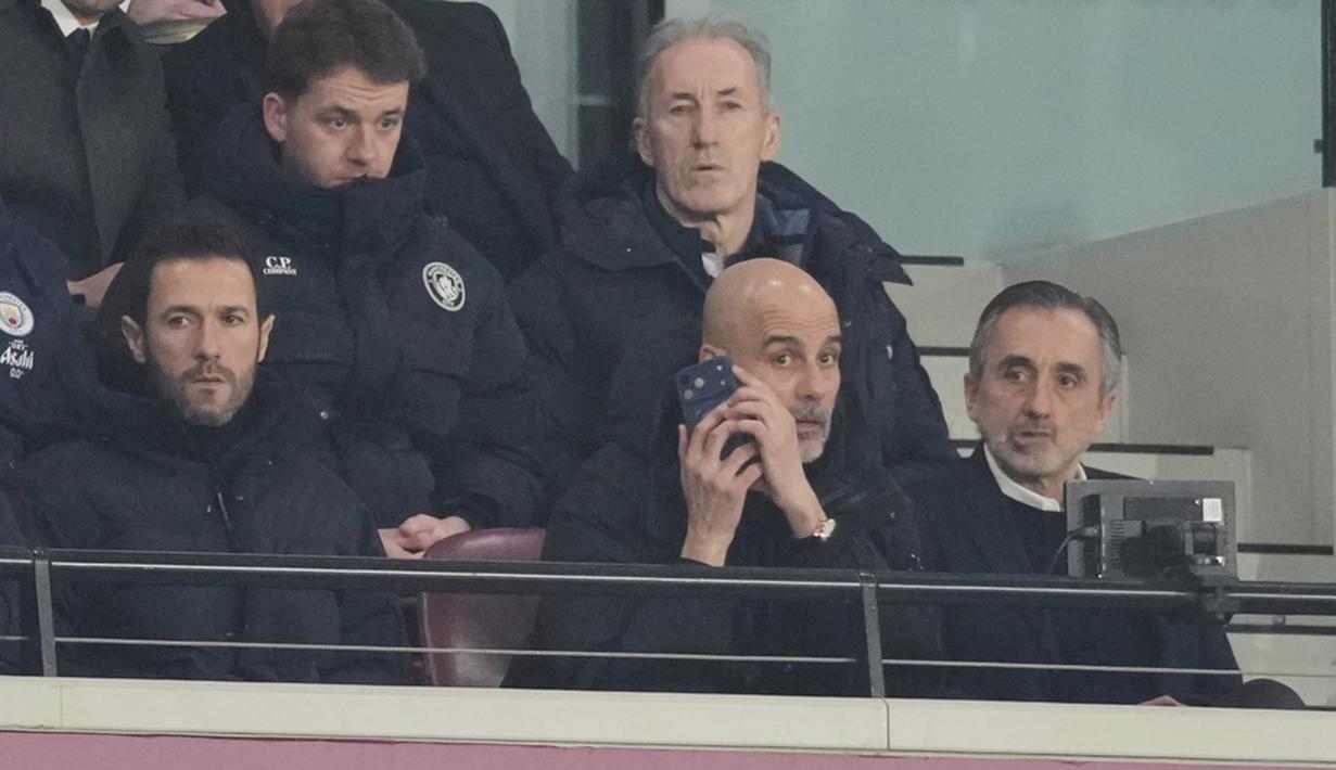 Pelatih Manchester City, Pep Guardiola, memberikan arahan melalui telpon dari tribun penonton saat anak asuhnya bermain imbang 1-1 melawan West Ham United pada pekan ke-30 Premier League 2025/2026 di London Stadium pada Minggu (15/3/2026). (AP Photo/Dave Shopland)