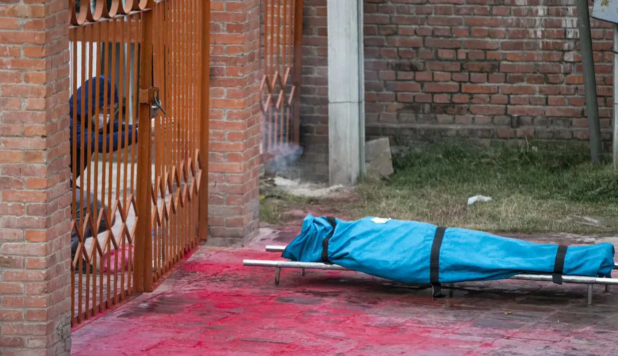 Seorang anggota keluarga berduka di samping mayat korban COVID-19 sebelum dikremasi di tepi Sungai Bagmati dekat kuil Pashupatinath di Kathmandu, Nepal (3/5/2021). Nepal juga membatasi pergerakan orang dan kendaraan serta menutup pasar, kantor dan sekolah. (AP Photo/Niranjan Shrestha)