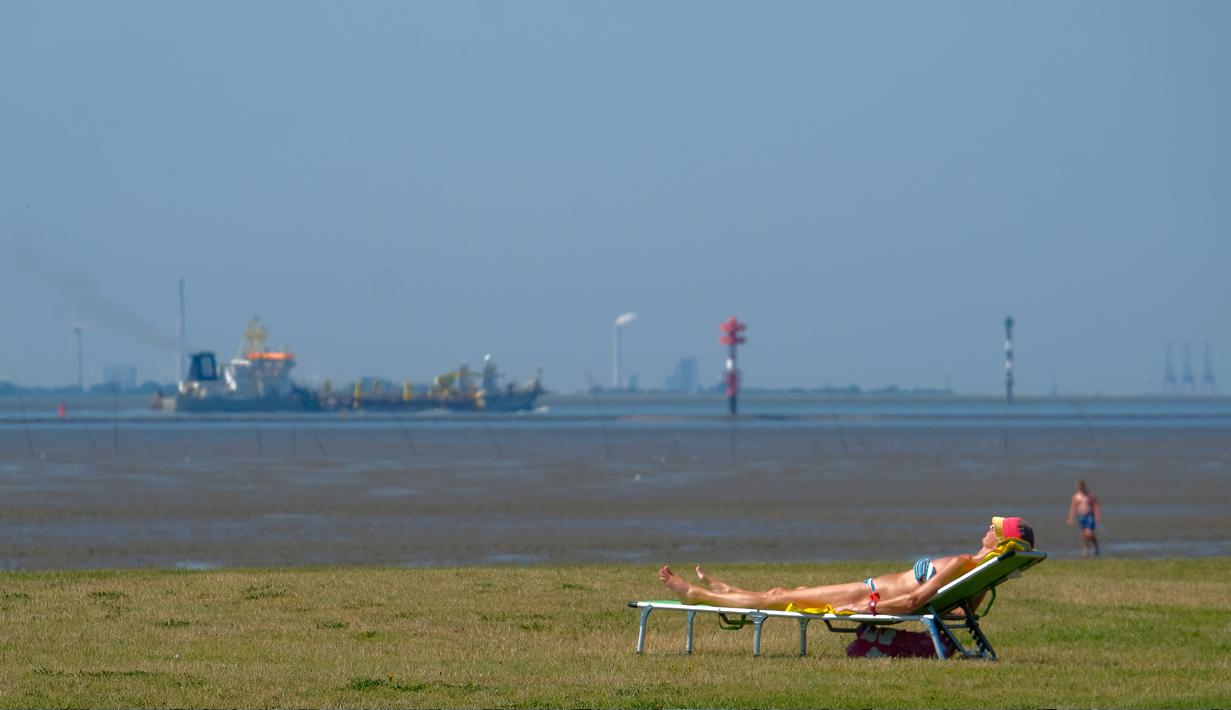Seorang wanita berjemur ketika kapal kargo menuju Laut Utara saat suhu mencapai 34 derajat Celcius di dekat pantai Laut Utara di Wremen, Jerman barat (24/7/2019). (AFP Photo/Patrik Stollarz)
