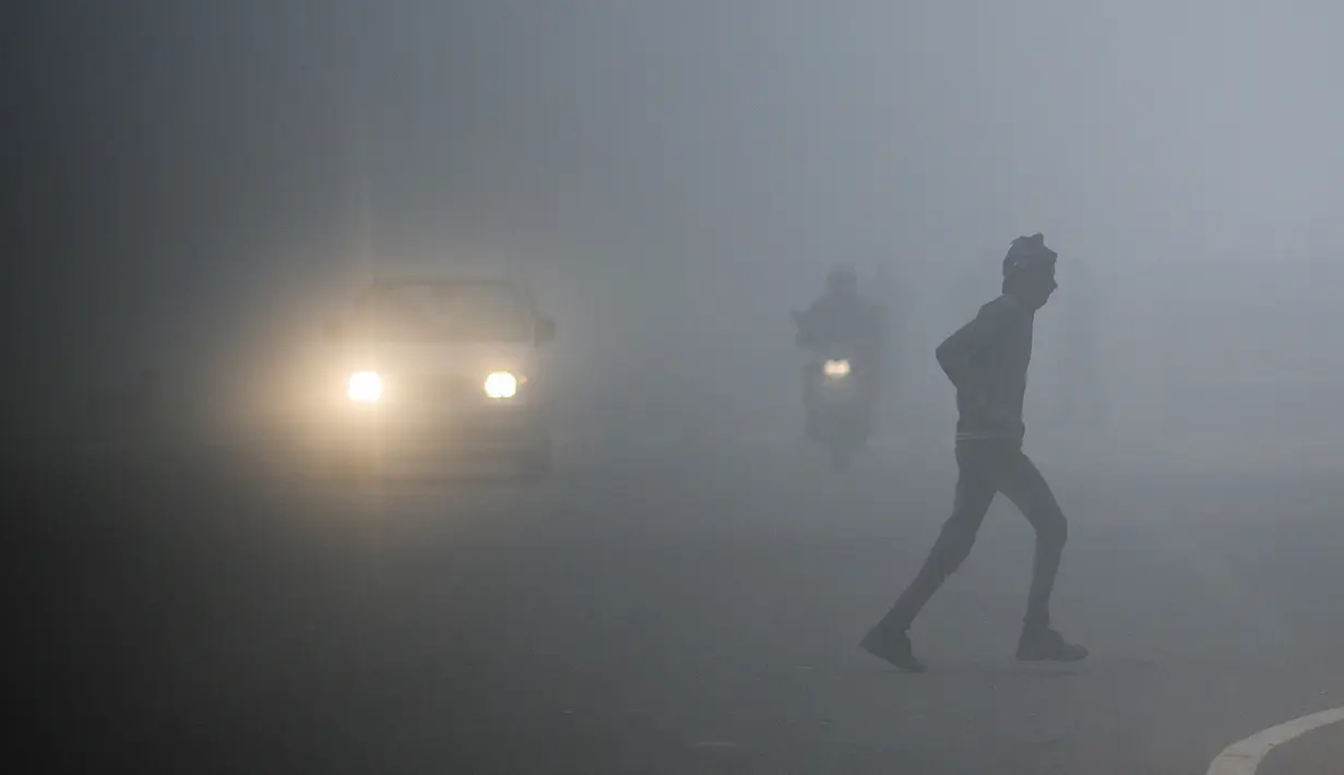 Seorang pria menyeberang jalan ketika kendaraan menembus kabut suhu dingin di New Delhi, Senin (30/12/2019). New Delhi, ibu kota India, saat ini mengalami musim dingin dengan hari dingin terpanjang dalam 22 tahun terakhir. (Photo by Jewel SAMAD / AFP)