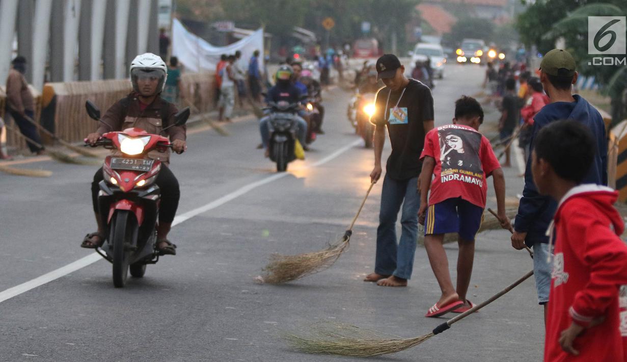 Warga membawa sapu menunggu pengguna jalan memberi sedekah dengan melempar uang di Jembatan Sewo, Jalur Pantura Sukra Indramayu, Jawa Barat, Senin (3/6/2019). Kehadiran pencari sedekah tersebut biasanya kian bertambah banyak saat menjelang arus mudik Lebaran. (Liputan6.com/Herman Zakharia)