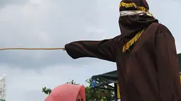 Nur Elita tampak meringis kesakitan saat petugas menyabetkan rotan ke punggungnya di halaman Masjid Baiturrahim, Ulee Lheue, Banda Aceh, Senin (28/12). Nur yang merupakan terpidana kasus khalwat mendapat hukuman 5 kali cambukan (AFP/dailymail.co.uk)