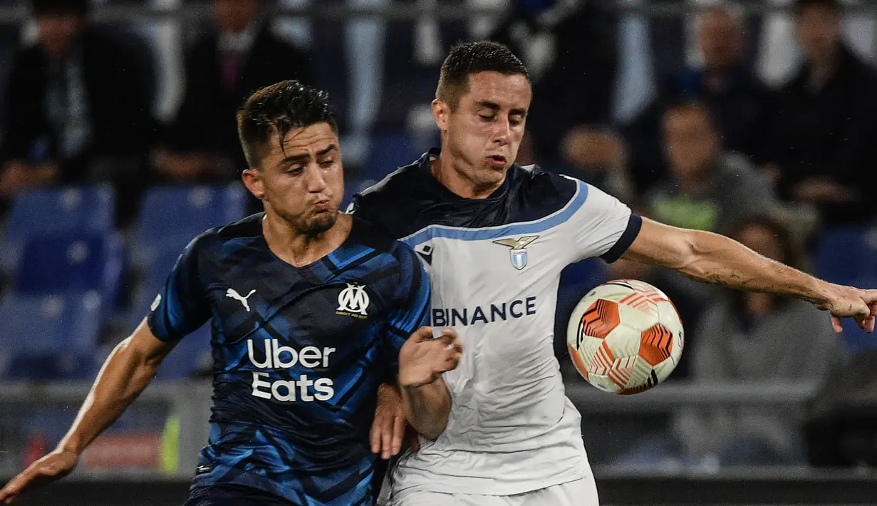 Penyerang Olympique Marseille, Cengiz Under (kiri) berebut bola dengan bek Lazio Adam Marusic pada matchday kedua Grup E Liga Europa 2021 di Stadion Olimpico Roma, Kamis (21/10/2021) malam WIB. Lazio hanya mampu bermain imbang 0-0 kala menjamu Marseille. (Filippo MONTEFORTE / AFP)