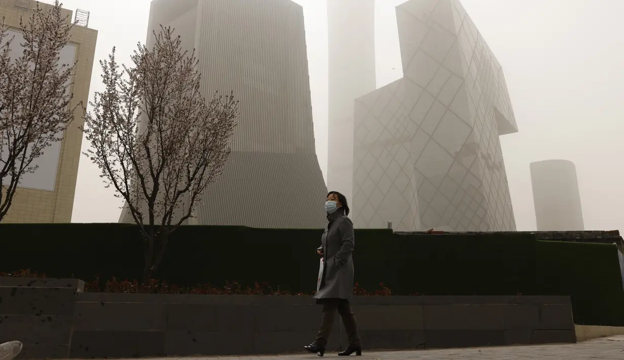 Seorang wanita melewati dekat gedung pencakar langit di Central Business District saat badai pasir di Beijing (28/3/2021). Sebelumnya Badai pasir menyapu Beijing, China pada Senin (15/3/2021) pagi.  (AP Photo/Ng Han Guan)