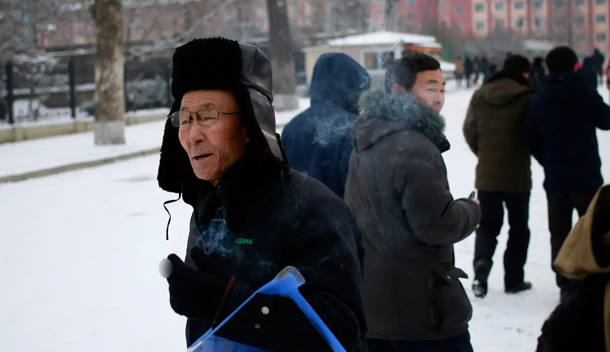Seorang pria mengisap  rokok saat melintasi jalanan tertutup salju di Pyongyang, Korea Utara Minggu (16/12). Korea Utara saat ini mulai memasuki musim dingin. (AP Photo/Dita Alangkara)