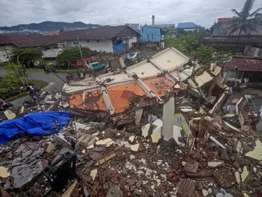 Pengemudi melewati bangunan yang diratakan oleh gempa bumi di Mamuju, Sulawesi Barat, Sabtu (16/1/2021). Petugas Badan Penanggulangan Bencana Daerah (BPBD) masih mendata jumlah kerusakan dan korban akibat gempa bumi tersebut. (AP Photo/Yusuf Wahil)