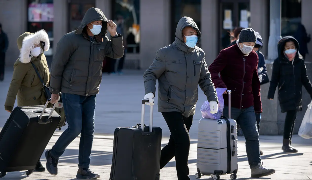 Wisatawan mengenakan masker berjalan dengan membawa barang bawaan mereka di Stasiun Kereta Api Beijing di Beijing, Kamis (28/1/2021).  Stasiun kereta api utama Beijing sebagian besar sepi pada hari pertama kesibukan perjalanan dan perkiraan jumlah penumpang lebih kecil daripada tahun-tahun sebelumny