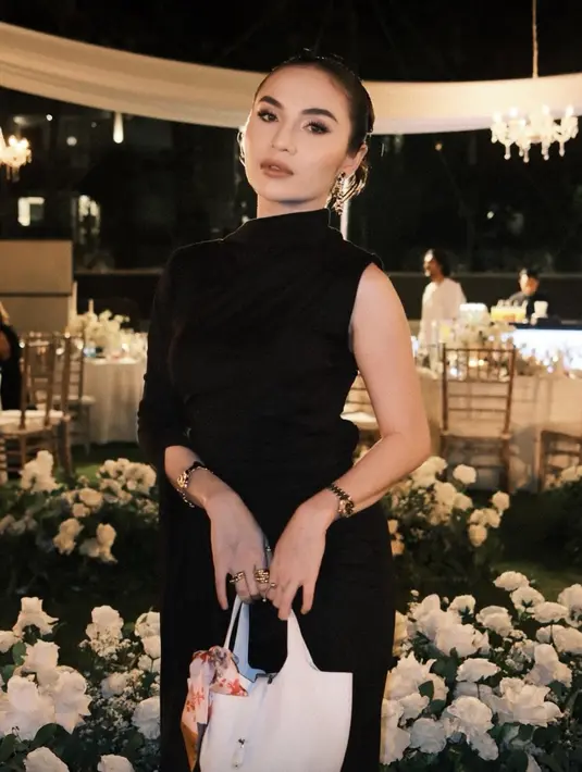 Elina Joerg tampil mengenakan dress hitam model lengan sleeveless dan long sleeves pada sisi lainnya. Dress kerah tinggi dipadukan handbag putih. [@elinaaaaajoerg]