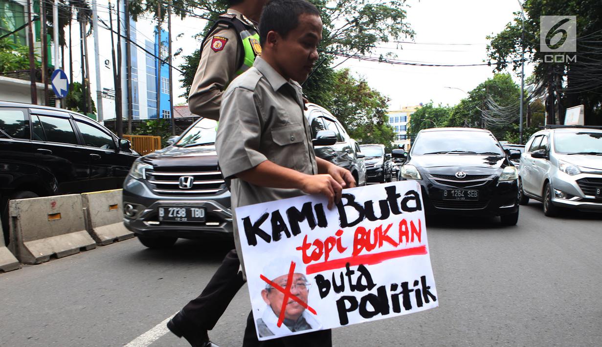 Seorang petugas polisi membantu penyandang disabilitas PASTI menyebrangi  jalan saat menggelar aksi di depan kantor Majelis Ulama Indonesia (MUI), Jakarta Pusat, Rabu (14/11). (Merdeka.com/Imam Buhori)