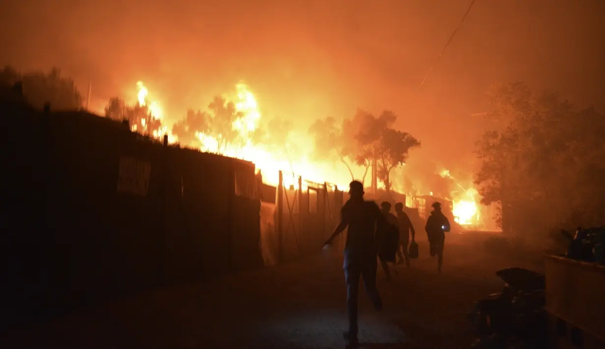 Pengungsi dan migran lari saat api membakar di kamp pengungsi Moria di timur laut pulau Aegean Lesbos, Yunani, Rabu (9/9/2020). Kamp tersebut digunakan sebagai tempat penampungan bagi para pengungsi dan imigran pencari suaka. (AP Photo/Panagiotis Balaskas)