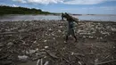 Seorang pria yang mengumpulkan bambu berjalan di antara sampah, termasuk sampah plastik, di Pantai Paparo di Negara Bagian Miranda, Venezuela, pada 6 Juni 2023. (Photo by Yuri CORTEZ / AFP)