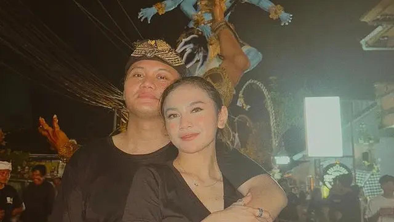Rizky Febian, bersama kekasihnya, mempesona dalam pawai ogoh-ogoh dengan paduan kaos hitam, kain biru di pinggang, dan hiasan kepala.&nbsp;