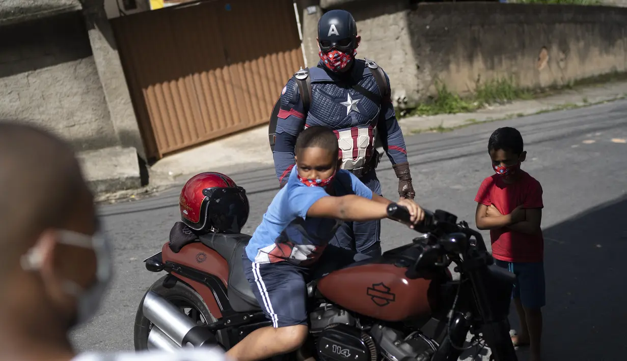 Seorang anak duduk di atas sepeda motor Everaldo Pinto, petugas polisi militer yang berkostum superhero Captain America di Petropolis, Rio de Janeiro, Brasil, Kamis (15/4/2021). Pinto memberitahu anak-anak tentang perlunya melindungi diri dari virus corona. (AP Photo/Silvia Izquierdo)