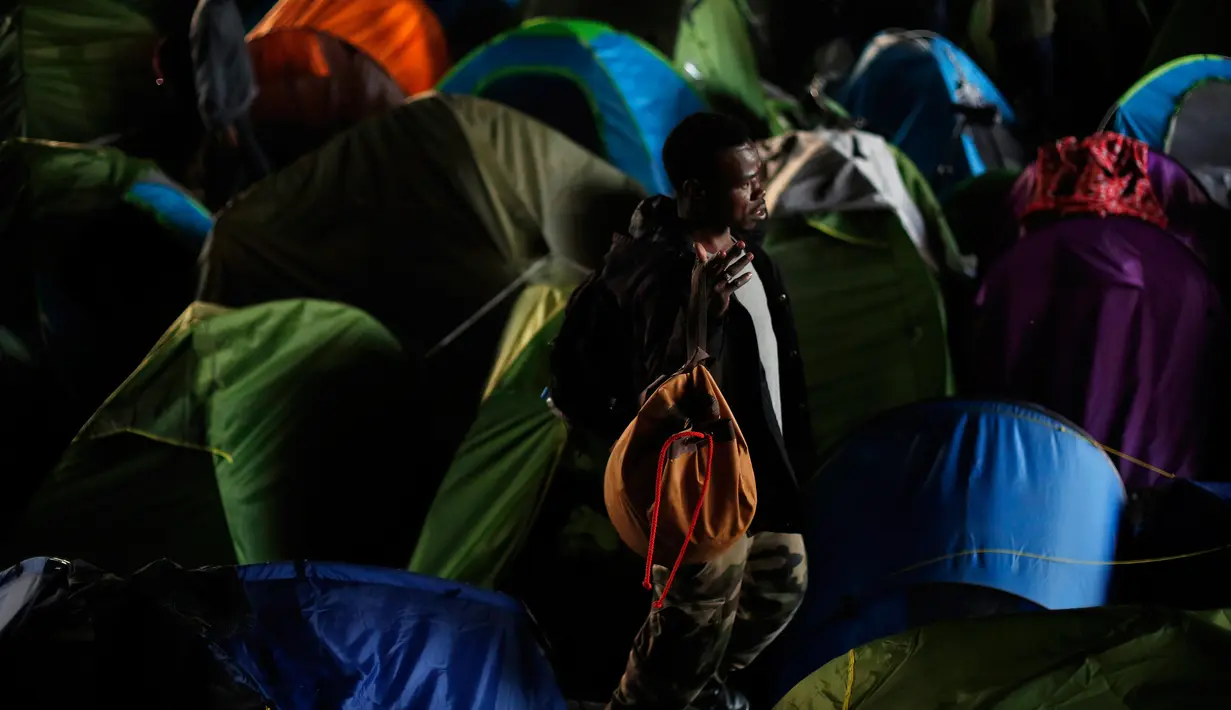 Seorang pria berjalan di sekitar tenda sementara di samping kanal di Paris, Prancis (30/5). Mereka yang menggelar tenda dibawan jembatan ini melebar hingga ke area pejalan kaki dan pengendara sepeda. (AP/Thibault Camus)