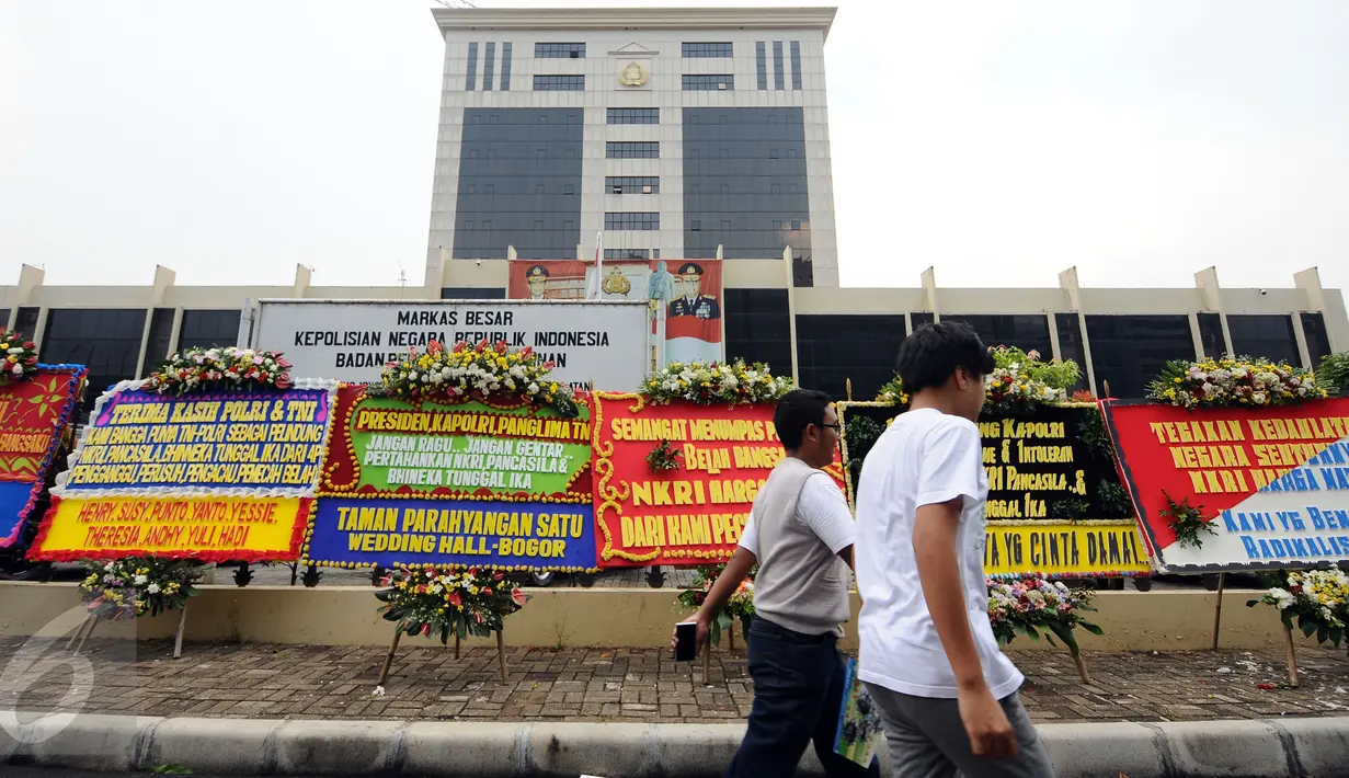 Warga melintasi deretan karangan bunga yang diletakkan di depan Mabes Polri, Jakarta, Rabu (3/5). Ratusan karangan bunga itu terus berdatangan dan mengelilingi gedung Mabes Polri di Jalan Trunojoyo Jakarta Selatan. (Liputan6.com/Helmi Fithriansyah)