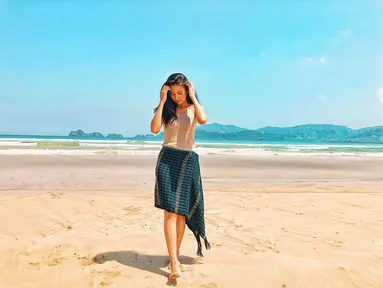 Penampilan dara kelahiran tahun 1997 ini sangat cerah saat berpose dengan latar belakang pantai pasir putih dan langit biru. Dengan baju berwarna putih dan Songket Bima berwarna gelap, tampak ia merapikan rambut hitamnya yang tergerai. (Liputan6.com/IG/indahpermatas)